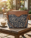 Floral-patterned bag with brown leather accents on a wooden table outdoors.