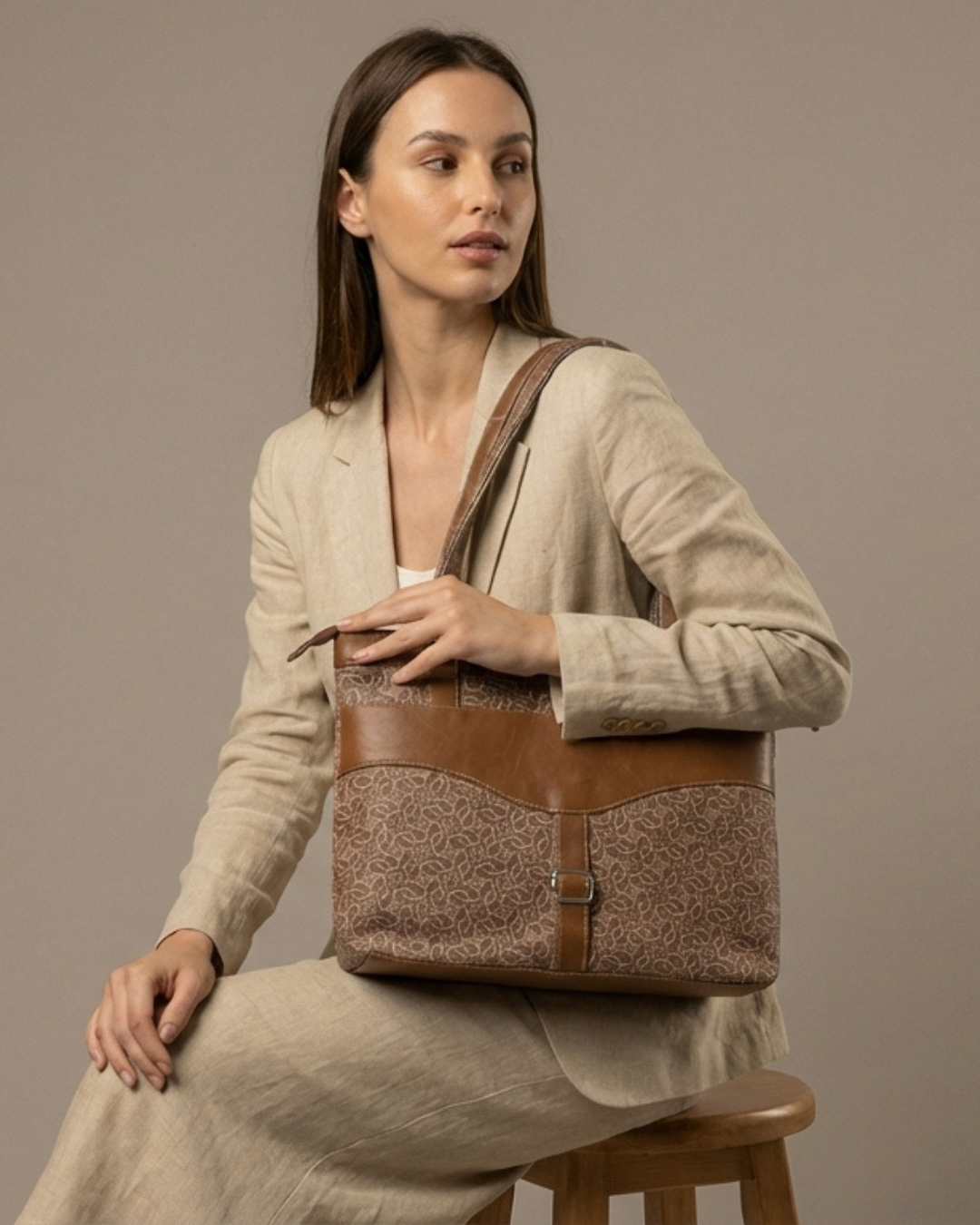 Woman holding a brown and beige handbag against a neutral background