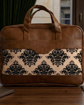 Brown leather briefcase with black floral pattern on a wooden surface