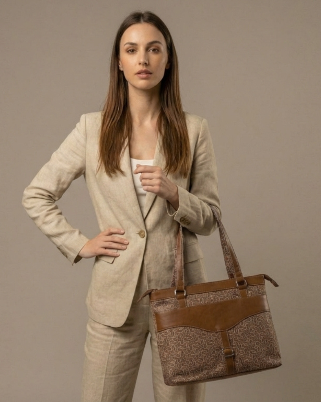 Woman in a beige suit holding a brown handbag against a neutral background