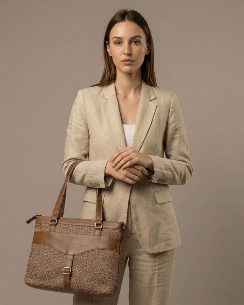 Woman in beige suit holding a brown textured handbag against a plain background