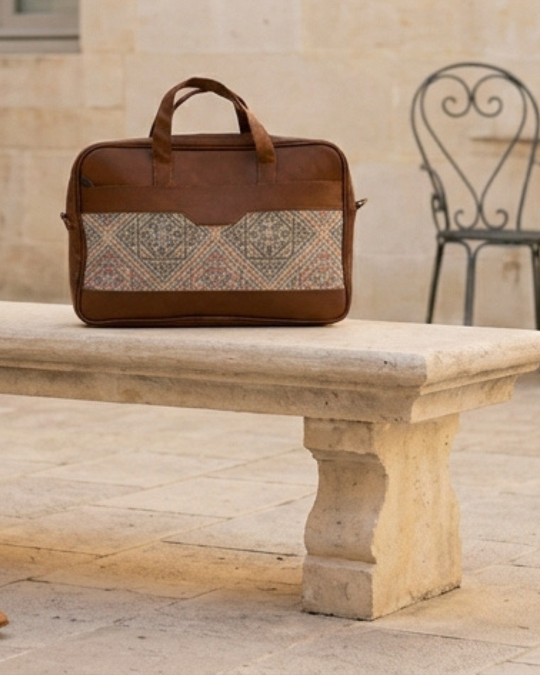 Brown leather briefcase with patterned flap on a stone bench outdoors
