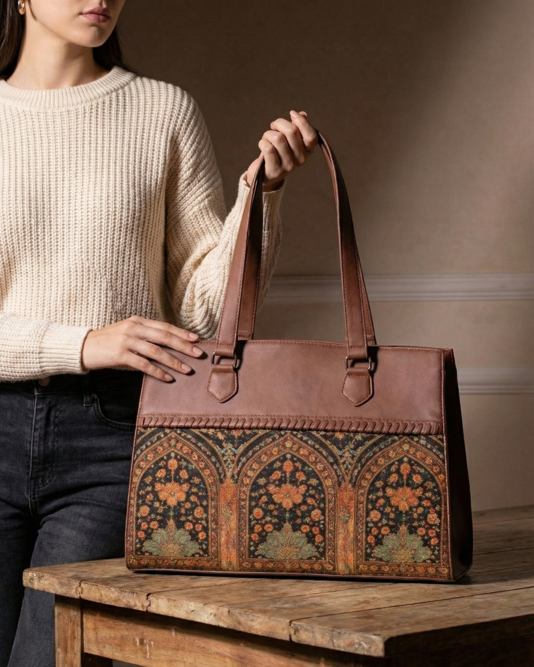 Person holding a brown leather bag with intricate patterns on a wooden surface.