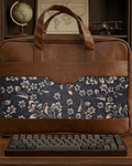 Brown leather and floral fabric briefcase on a wooden surface with a keyboard in front.