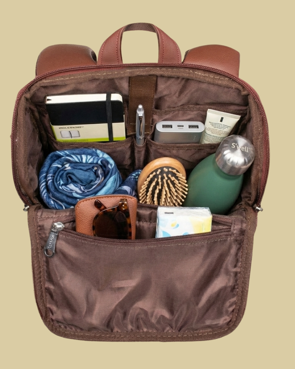Brown backpack with various items including a water bottle, sunglasses, and toiletries on a beige background