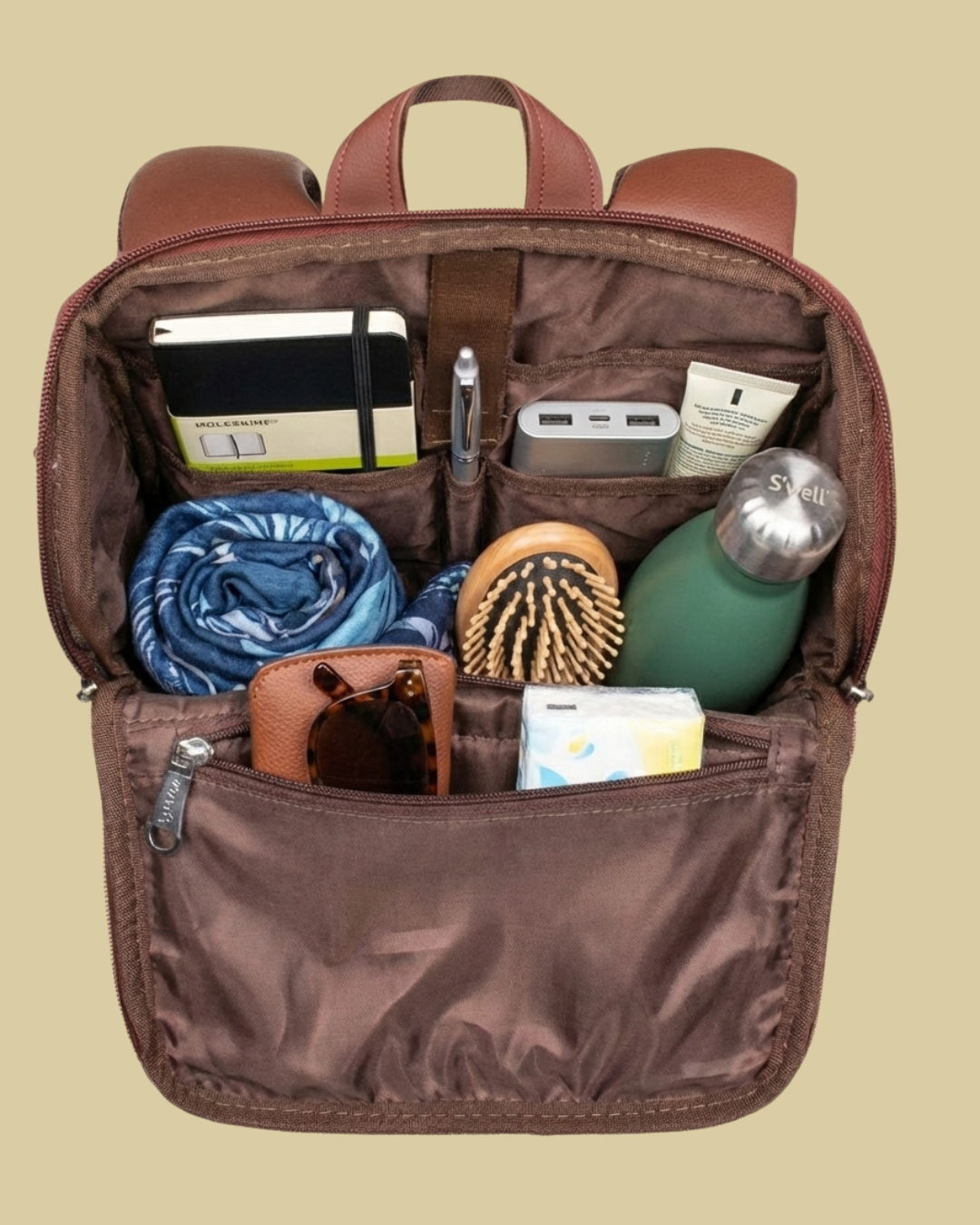 Brown backpack with various items including a water bottle, sunglasses, and toiletries on a beige background